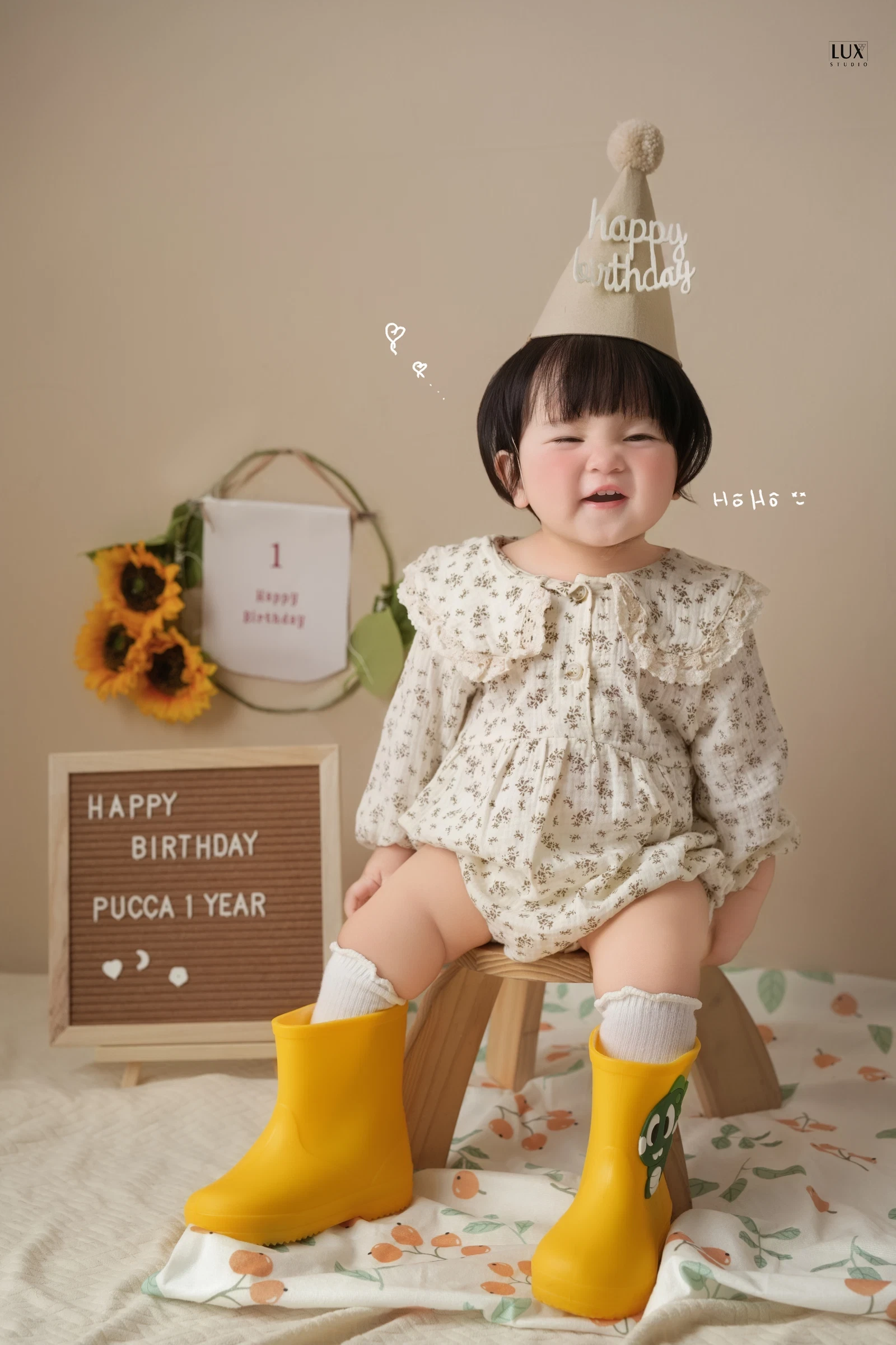 Bé trai đội mũ sinh nhật ngồi bên bảng tên