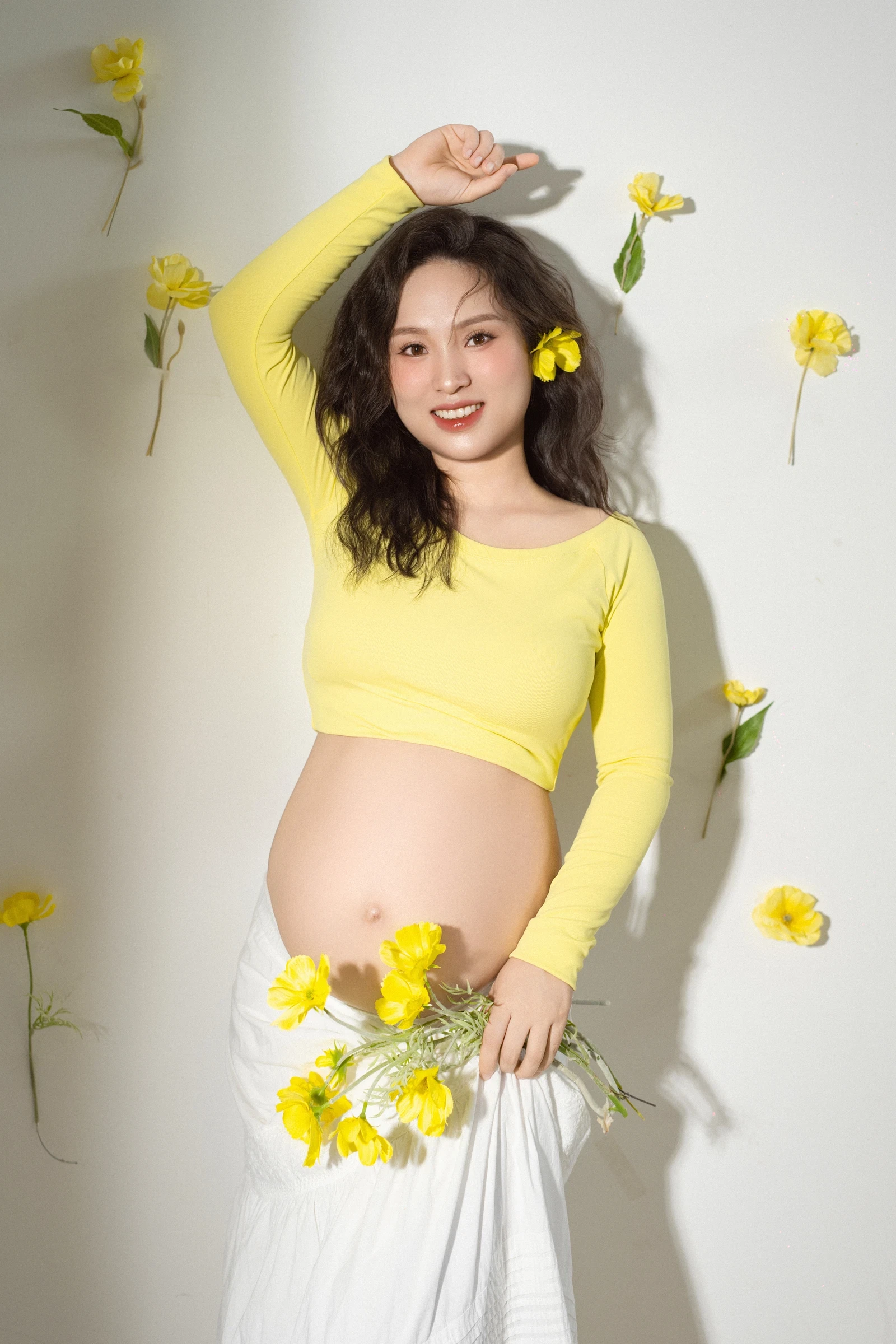 Mẹ bầu áo vàng cầm hoa trước phông trắng