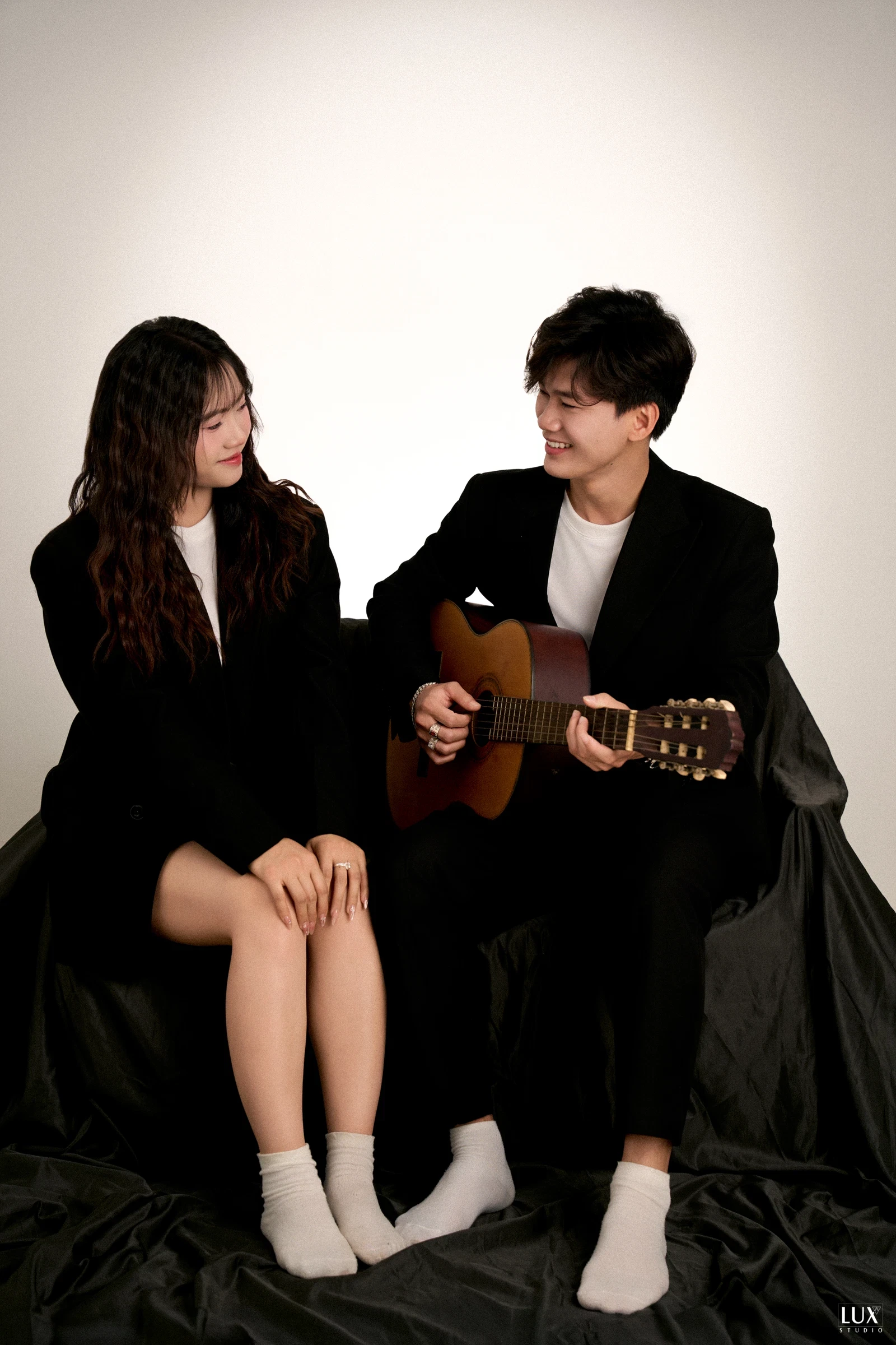 Cặp đôi đồ đen ngồi đàn guitar trong studio