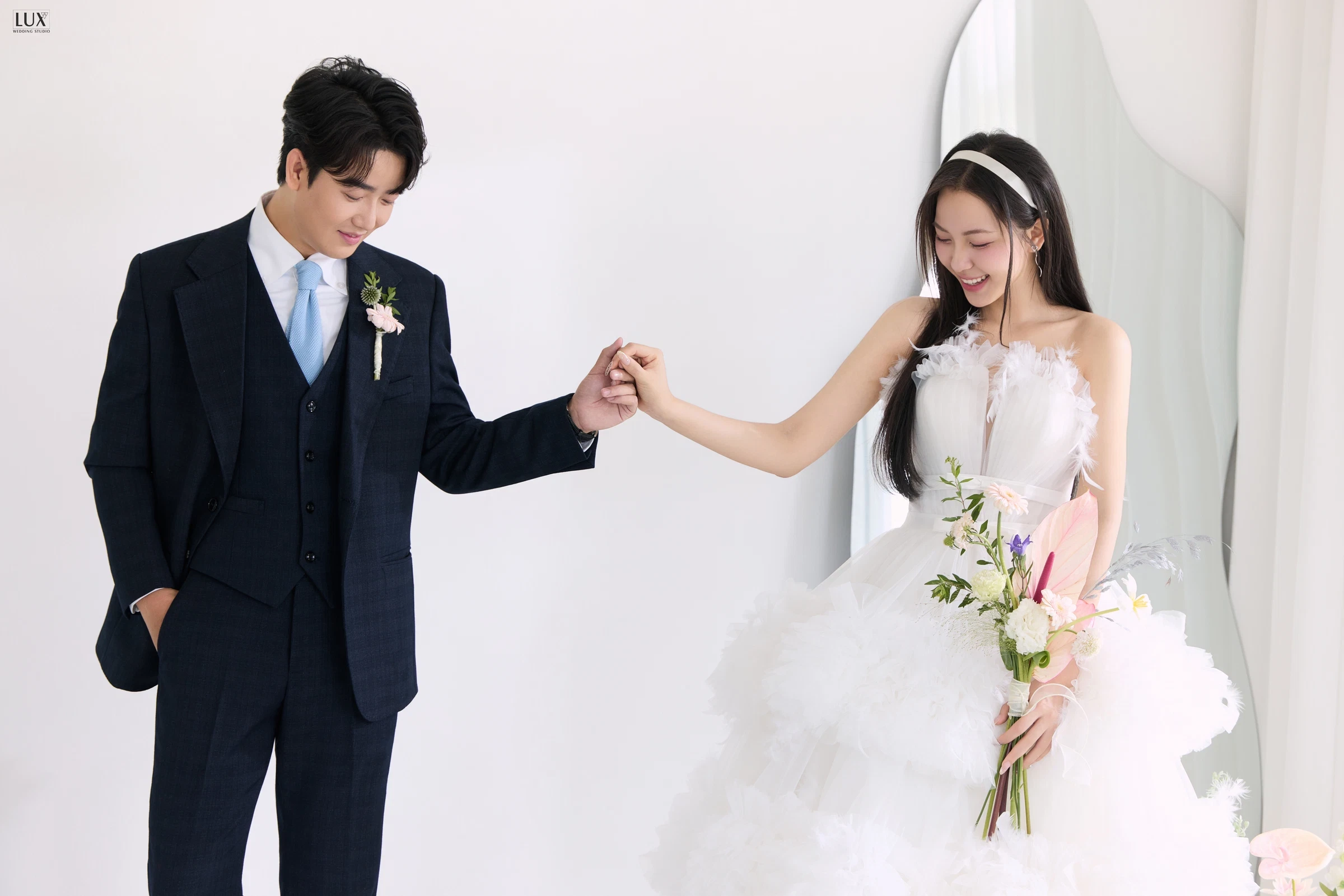 Chú rể vest xanh đậm nắm tay cô dâu váy bồng trong studio