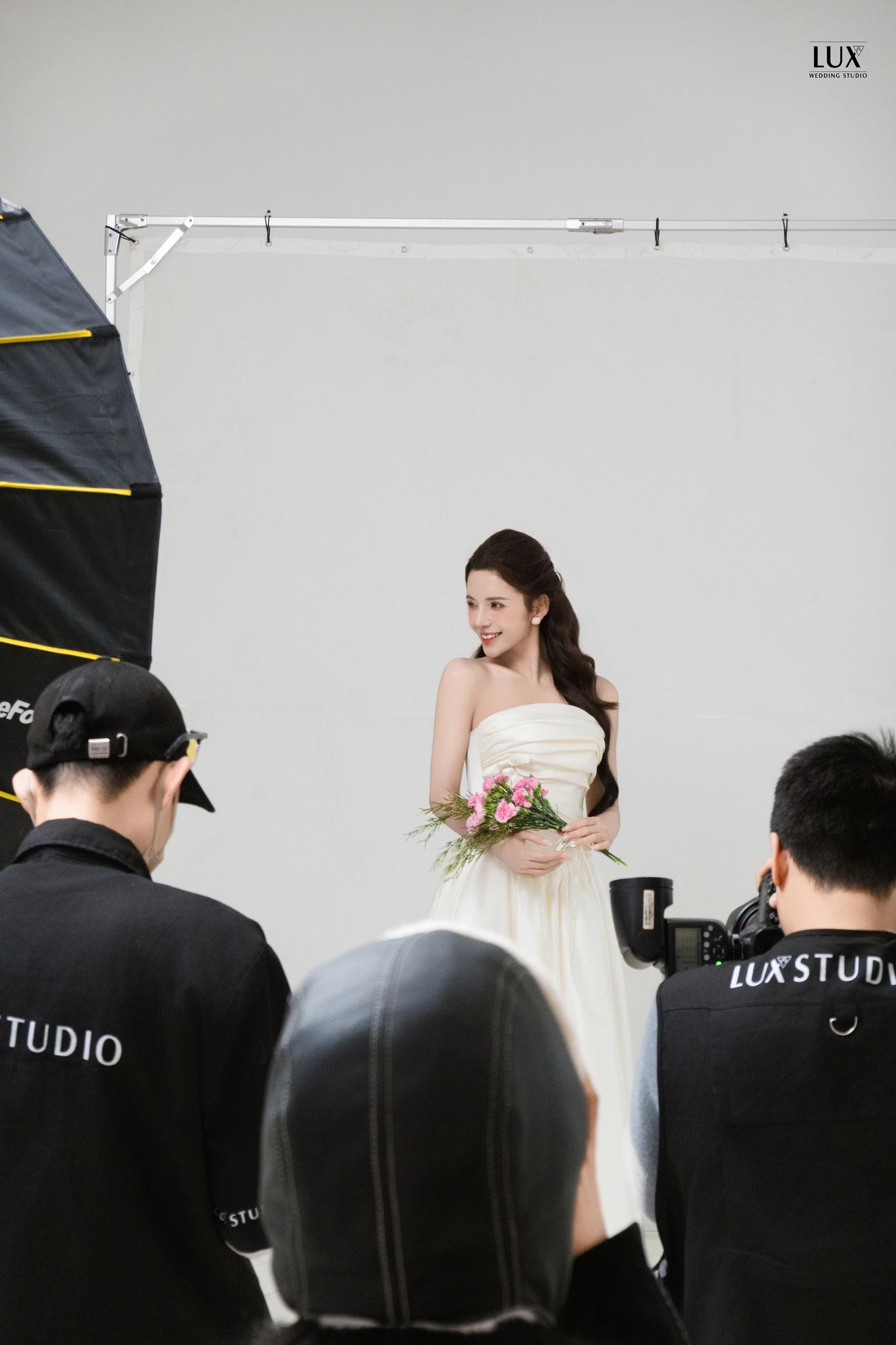 Ekip LUX Studio mặc áo đồng phục đen đang chụp ảnh cô dâu cầm hoa hồng trong studio phông trắng