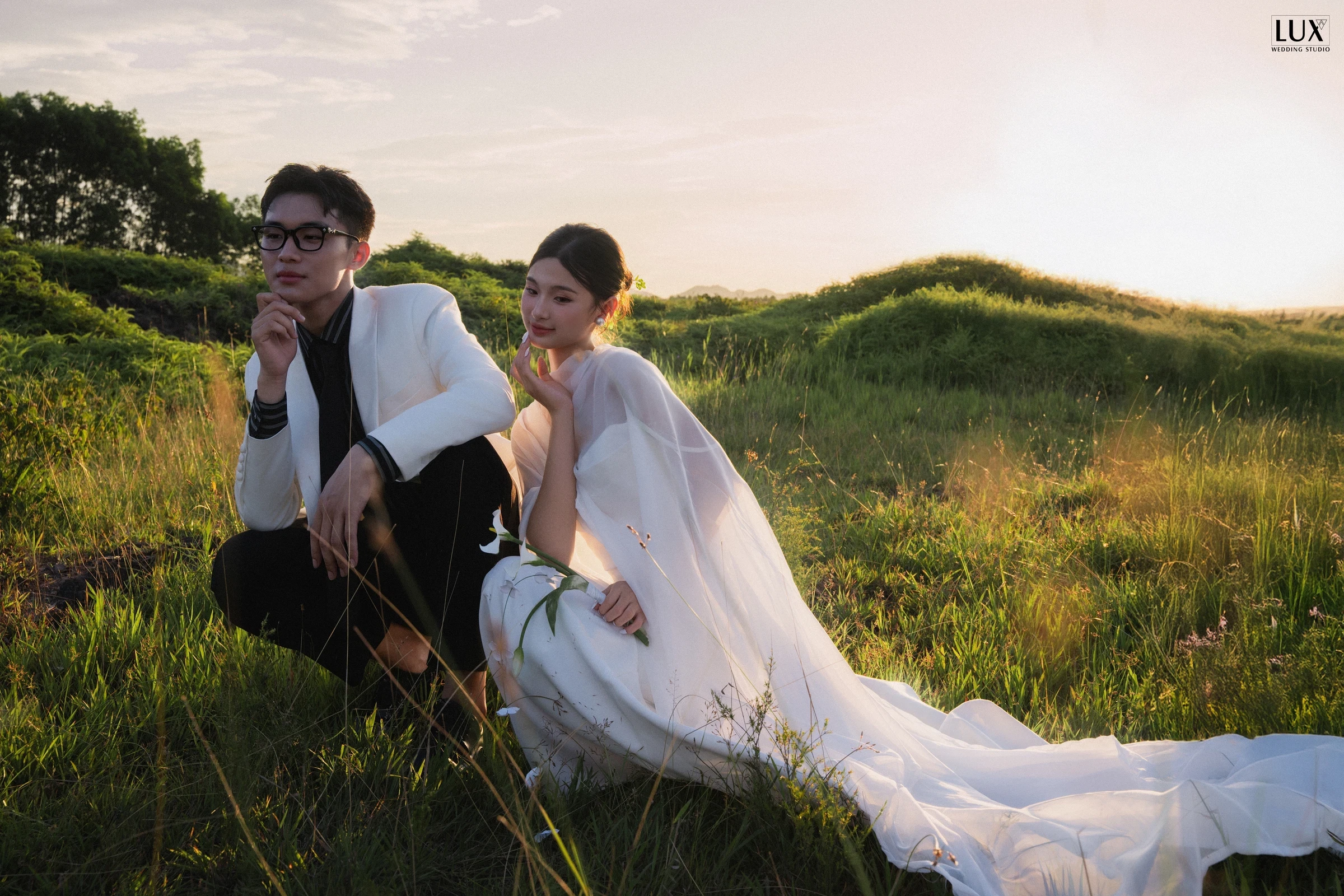 Cặp đôi ngồi giữa đồng cỏ lúc hoàng hôn