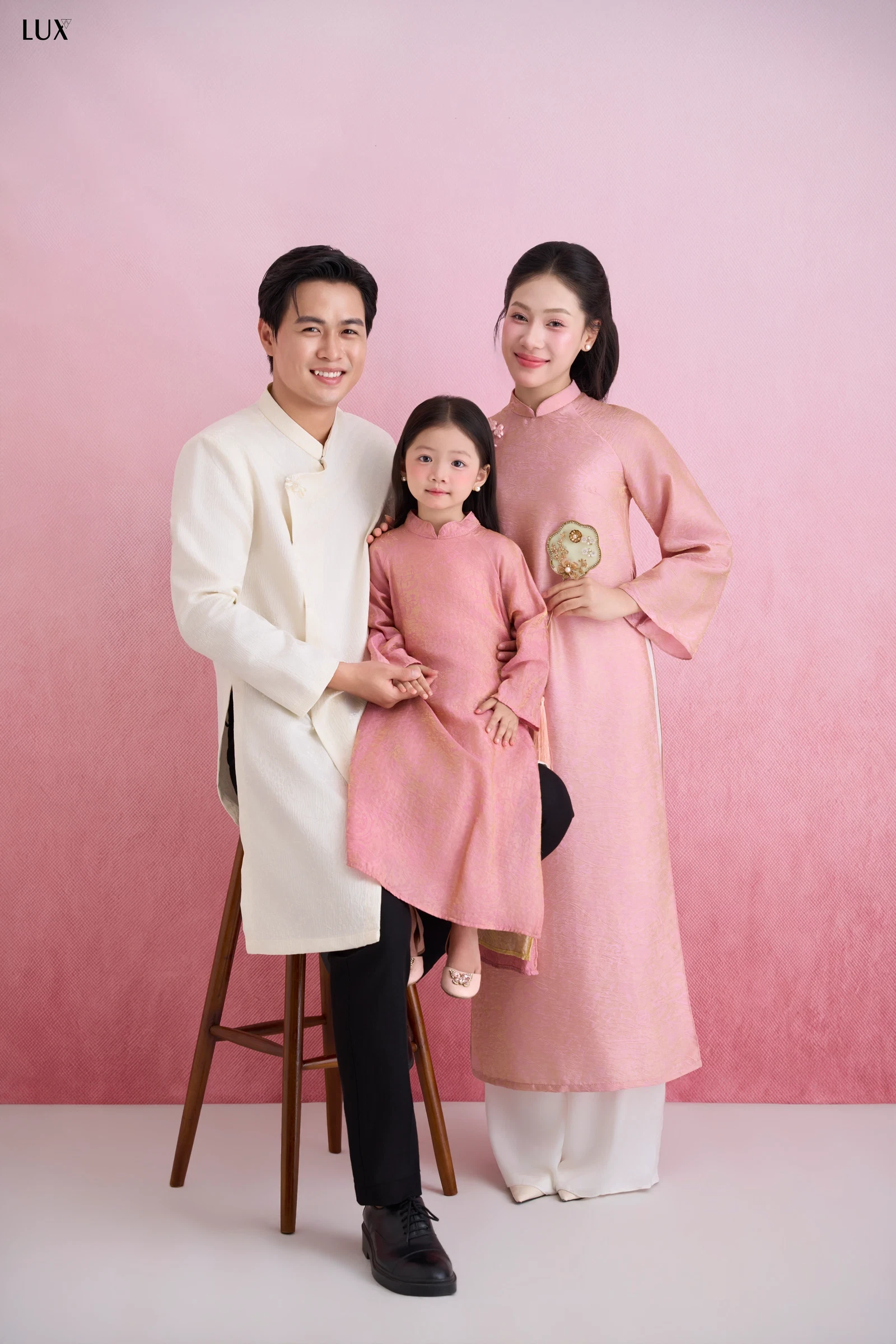 Gia đình ba người mặc áo dài trước phông hồng
