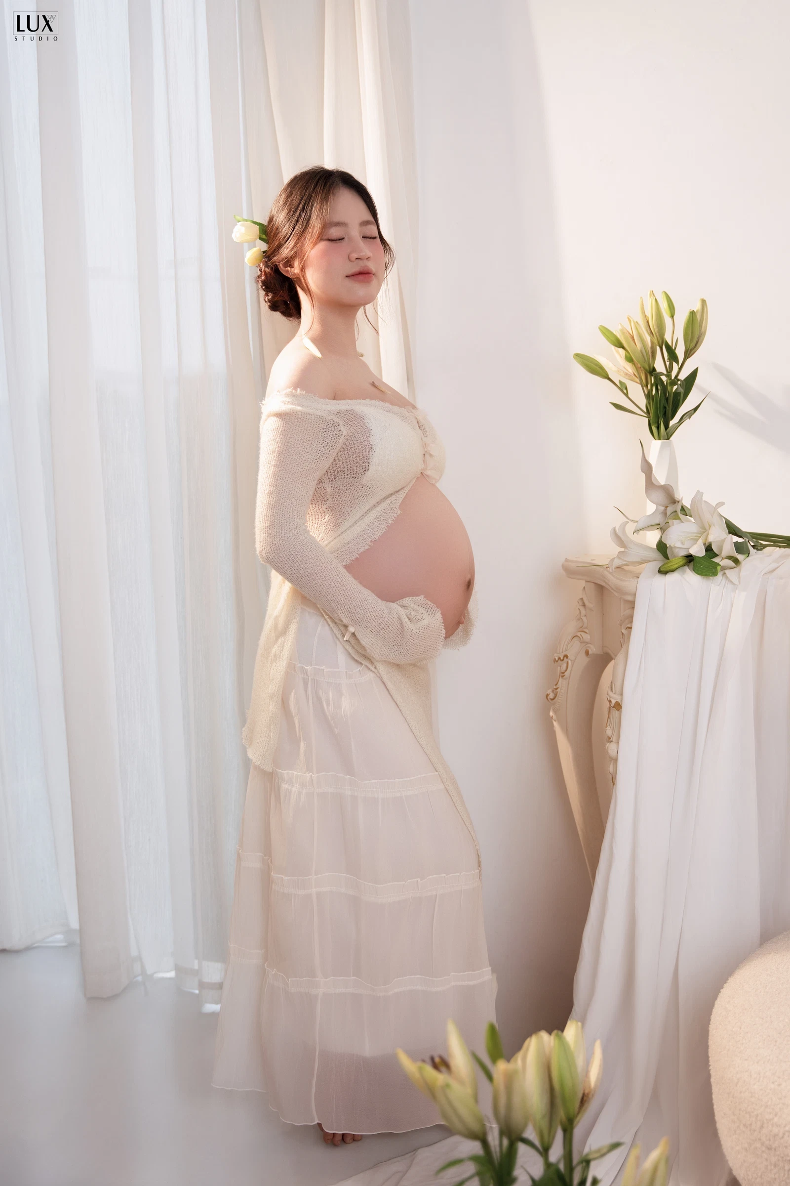 Mẹ bầu váy ren trắng đứng bên cửa sổ