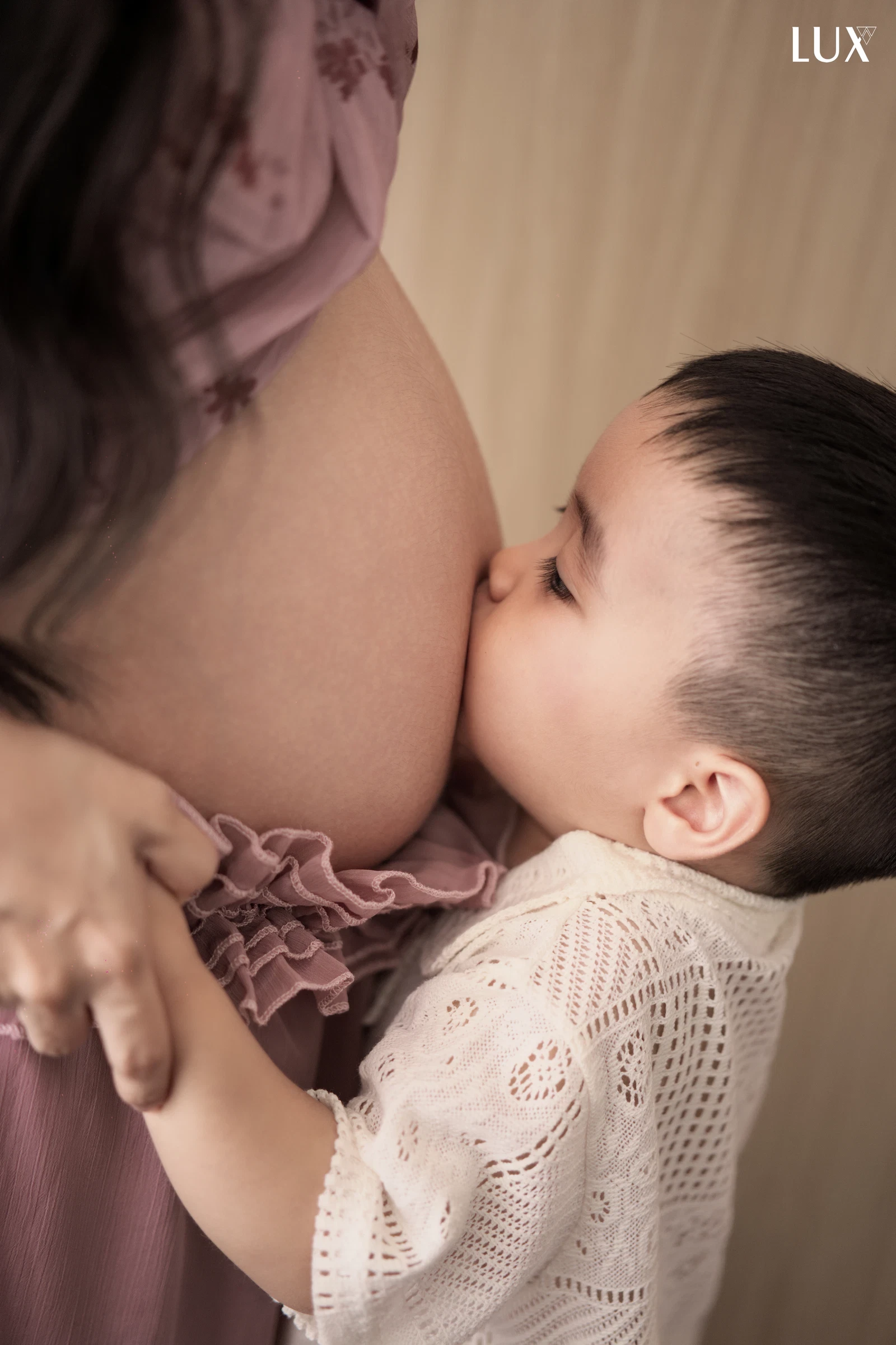 Bé trai mặc áo ren trắng ôm và hôn lên bụng bầu của mẹ